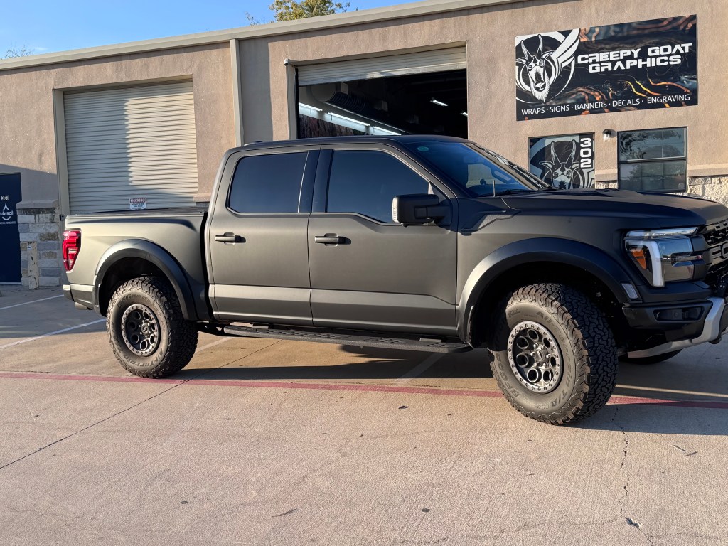 A matte black wrapped Dord Raptor sitting in front of Creepy Goat Graphics with shop sign above the main door. 